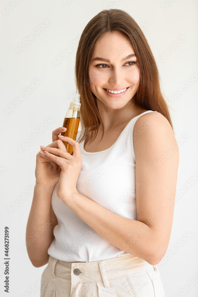 Fototapeta premium Happy woman holding spray bottle with essential oil on light background