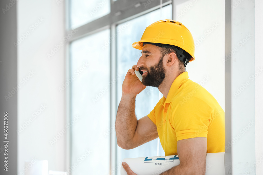 Construction worker talking by mobile phone near window in room Construction worker talking by mobile phone near window in room