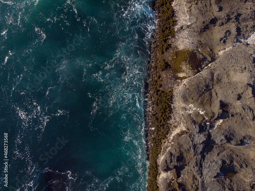 Aerial view. Seascape. Dark turquoise ocean water with white foamy waves and uneven, rough rocky shoreline. Environmentally friendly place, environmental protection.