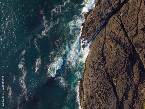 Drone shot. Seascape. Raging waves, dark turquoise ocean water and dark brown rocky shore. Abstraction. Minimalism. The greatness and beauty of nature.