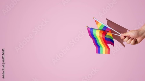 hairy hand of a man holding rainbow flag above a pink background. hard shadows of the sun, vertical orientation, copy space