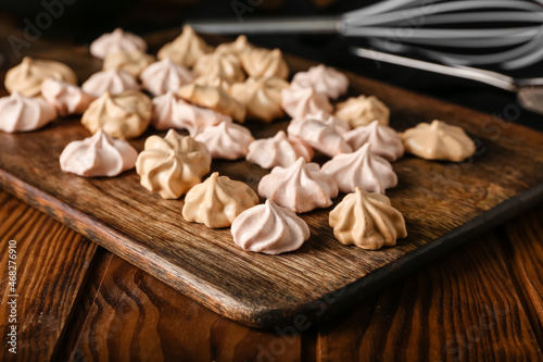 Board with tasty meringues on wooden background