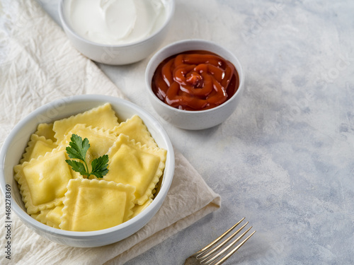 A portion of Italian ravioli with a parsley leaf on top and two sauces - tomato and sour cream on a white plate. Italian food. Restaurant, hotel, cafe, home cooking, cookbook.