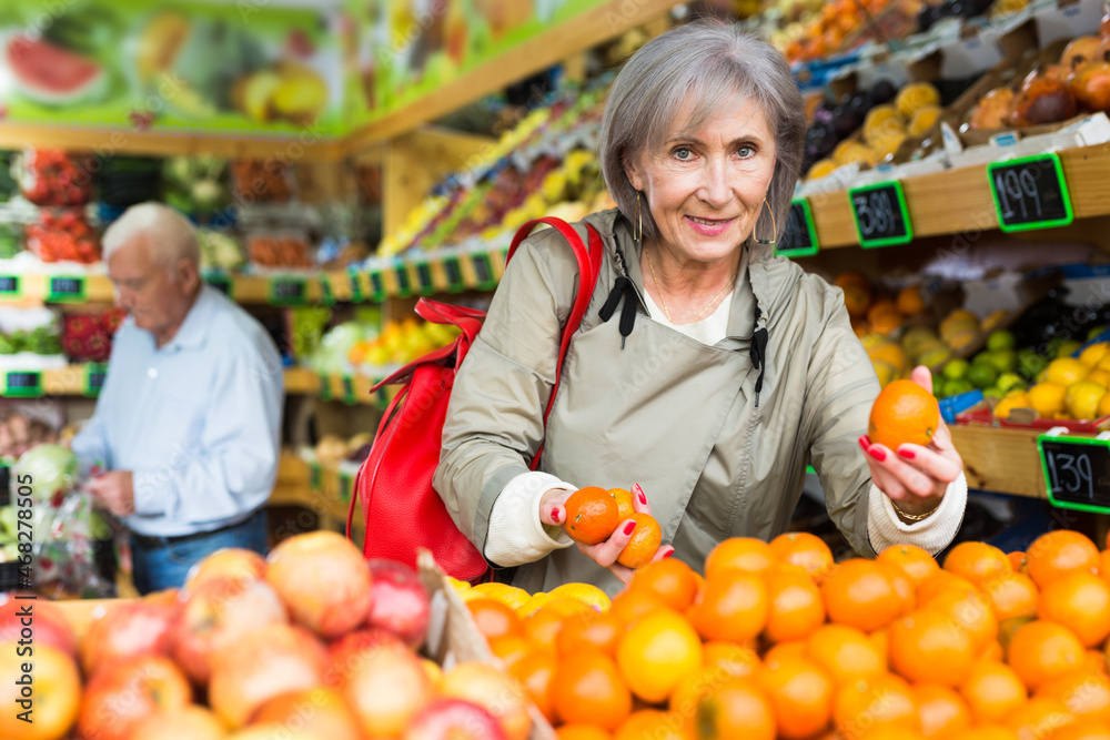 Woman selecting tangerines in greengrocer. Man walking in background