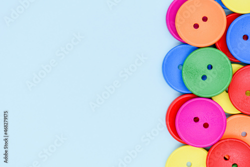Vivid colored wooden buttons on blue background. Bright multicolored round buttons border close up. Eco recycle sewing and needlework concept with copy space.
