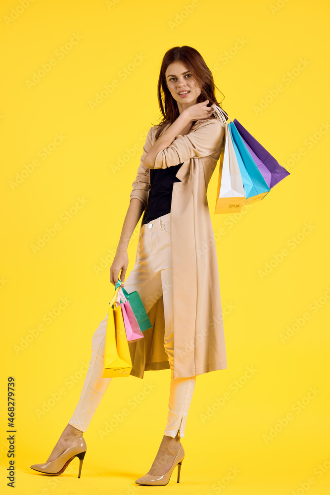 cheerful woman with multicolored bags posing yellow background