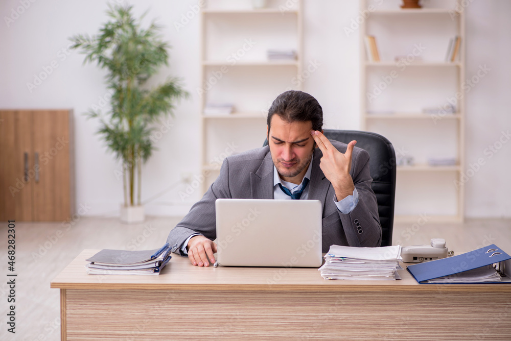 Young male employee unhappy with excessive work in the office Young male employee unhappy with excessive work in the office