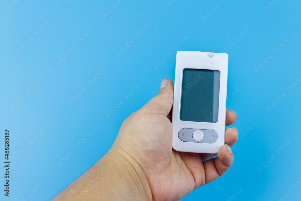 Digital glucometer in female hand over a pastel blue background. Diabetes concept Digital glucometer in female hand over a pastel blue background. Diabetes concept