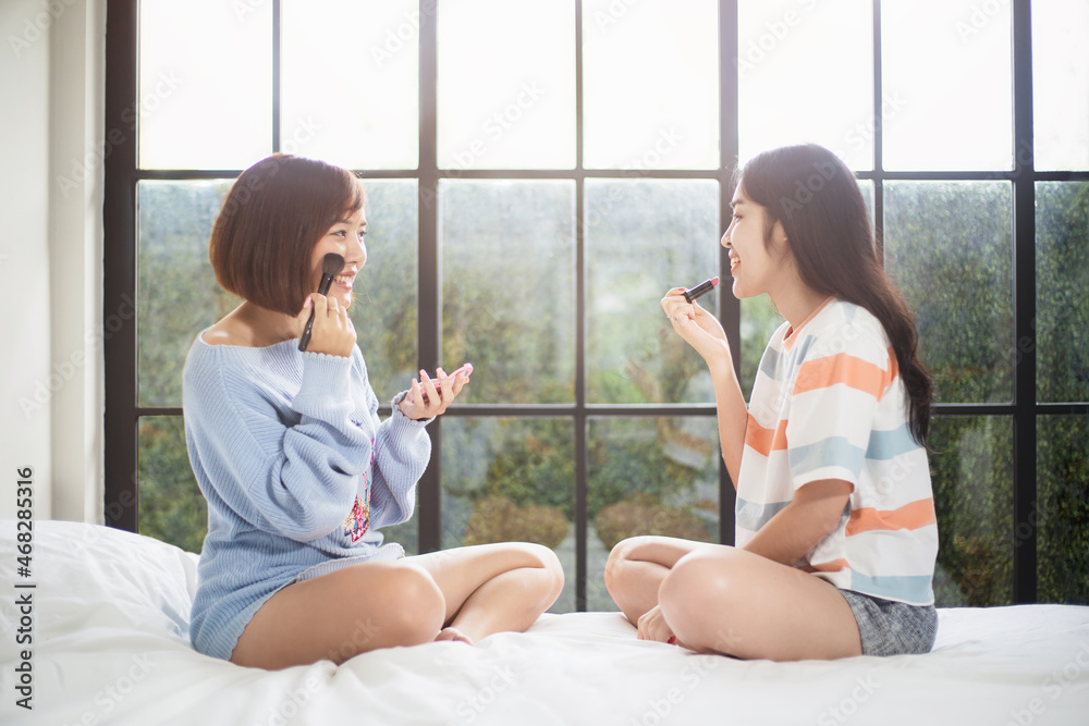 Two Asian teenage girls having fun while applying make up on the bed in the morning Two Asian teenage girls having fun while applying make up on the bed in the morning