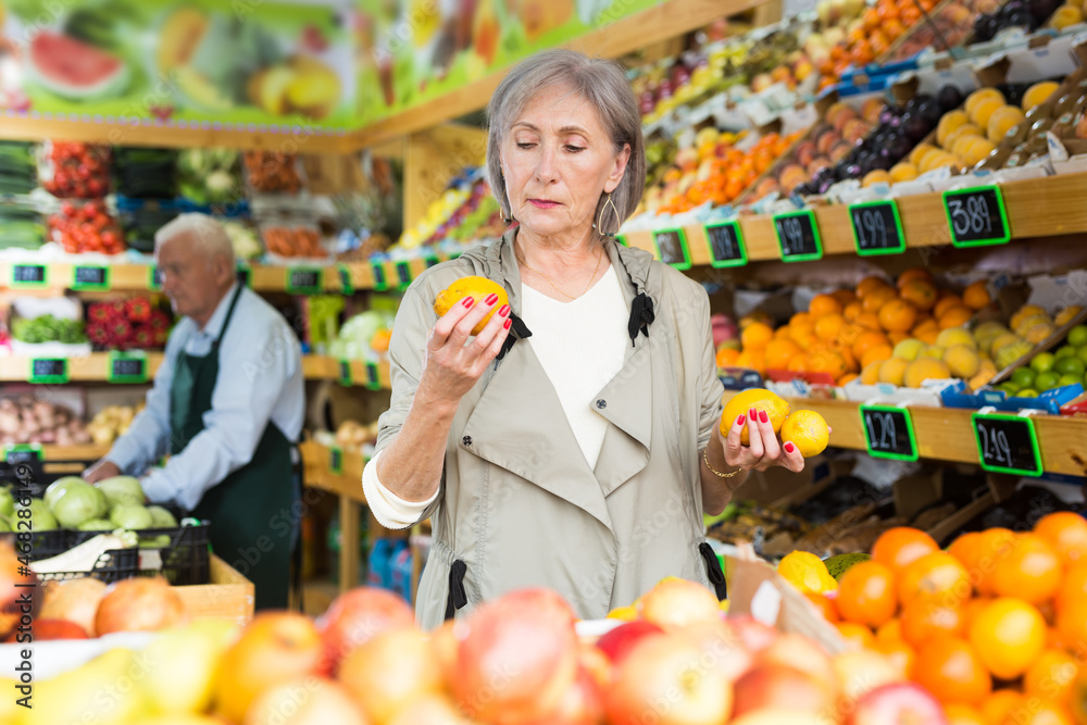 Positive female buyer shopping in supermarket, choosing ripe apples in fruit and vegetable department
