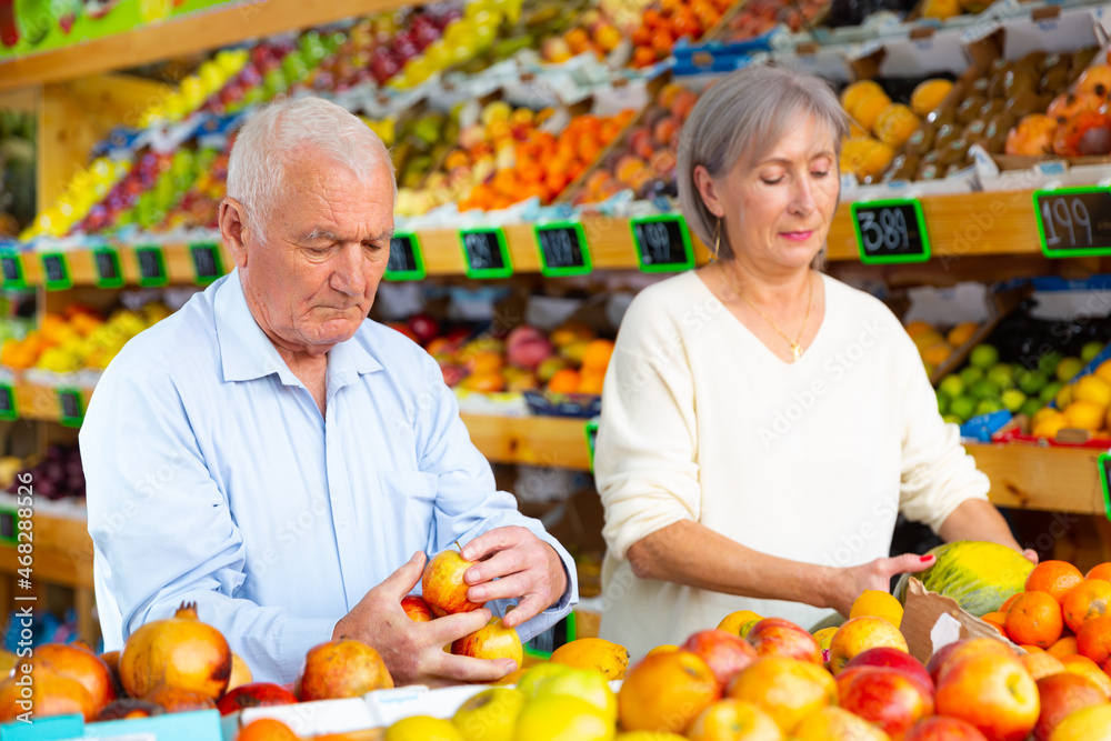 European old man and woman choosing fresh fruits in greengrocer.