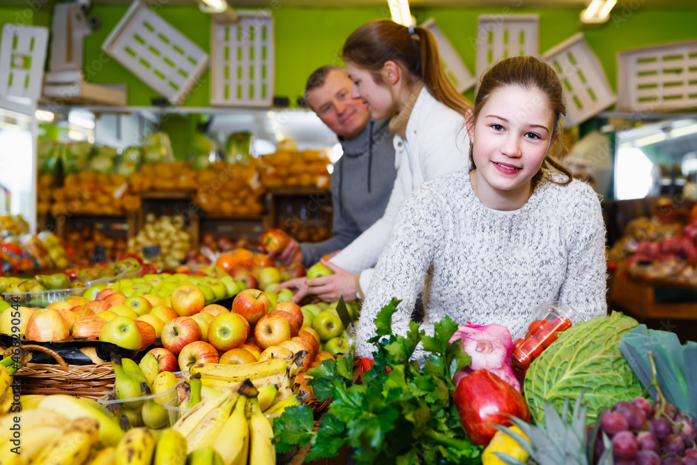 Cheerful little girl with loving parents choosing fresh fruits and vegetables in market