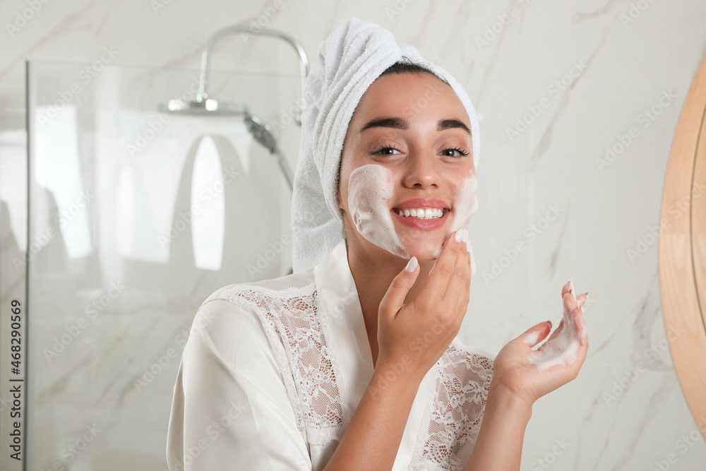 Beautiful young woman applying cleansing foam onto face in bathroom. Skin care cosmetic Beautiful young woman applying cleansing foam onto face in bathroom. Skin care cosmetic