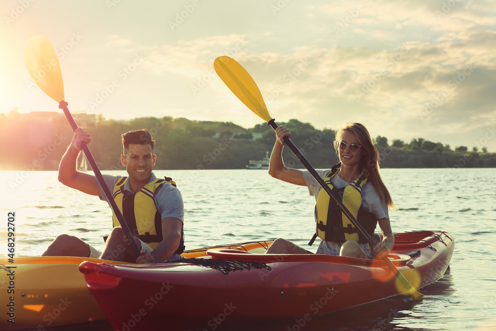 Couple in life jackets kayaking on river at sunset. Summer activity
