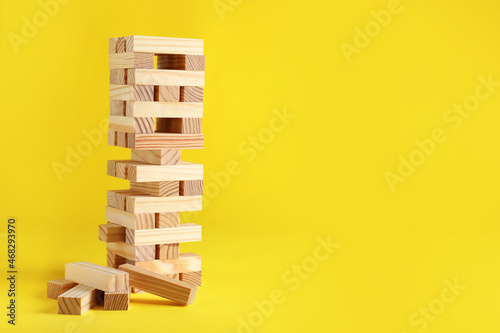 Jenga tower made of wooden blocks on yellow background, space for text photo