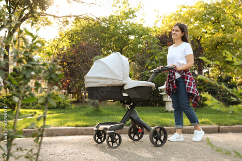 Happy mother with baby in stroller walking in park on sunny day photo