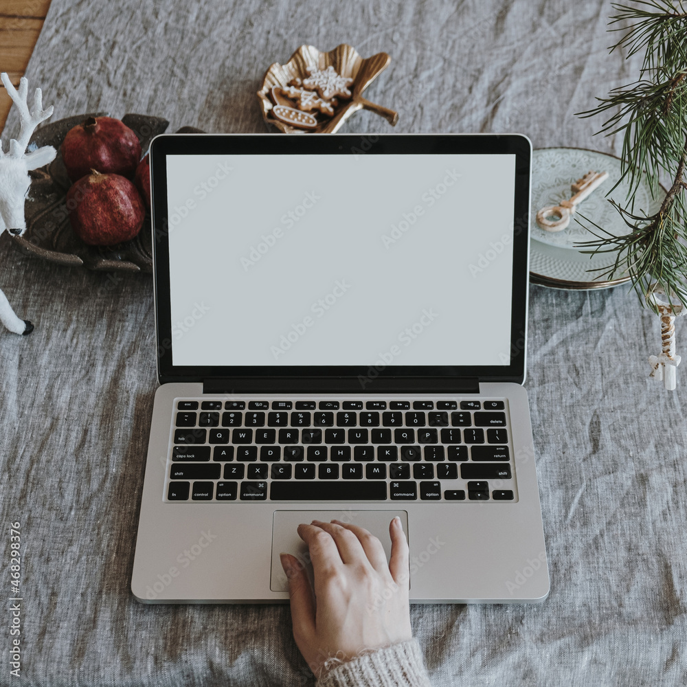 Female hand on laptop computer with blank copy space screen. Comfortable  aesthetic home office desk workspace with linen table cloth decorated for  Christmas with fir needles. Work at home Stock Photo