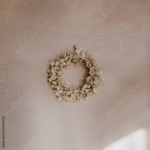 Fototapeta Naklejka Na Ścianę i Meble -  Gold Christmas wreath made of natural dry lunaria leaves hanging on a pink wall with sunlight shadows. New Year and winter holidays. Aesthetic Christmas decor