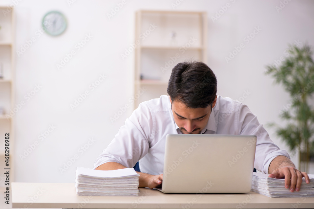 Young male employee unhappy with excessive work in the office Young male employee unhappy with excessive work in the office