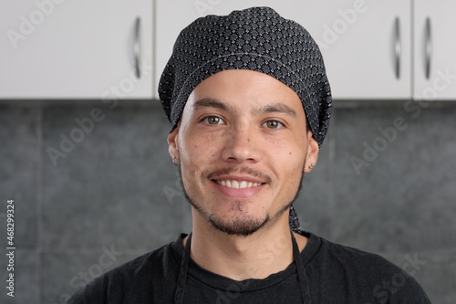 close-up portrait of young Latin American man in chef's hat, looks at camera and smiles.
