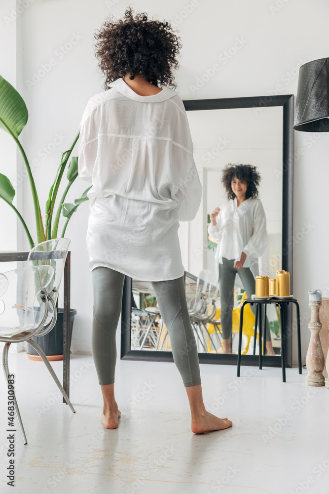 © Daniel - Young pretty mixed race woman with curly hair looking at herself in mirror. Checking out her outfit.