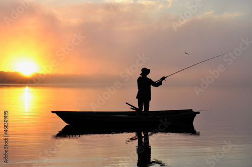 Lonely fisherman in the boat fishing on the misty river during sunrise
