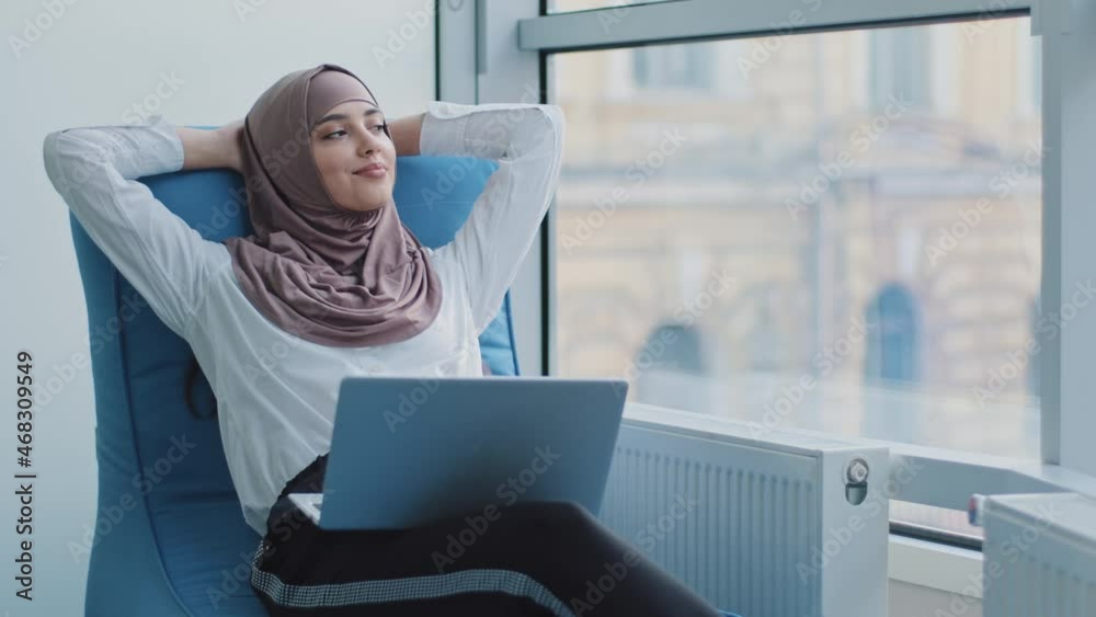 Relaxed beautiful muslim arabic businesswoman worker sits in comfortable armchair meditating, positive calm Arabic woman relax hold hand behind head dream rest from computer stretch feel peace of mind