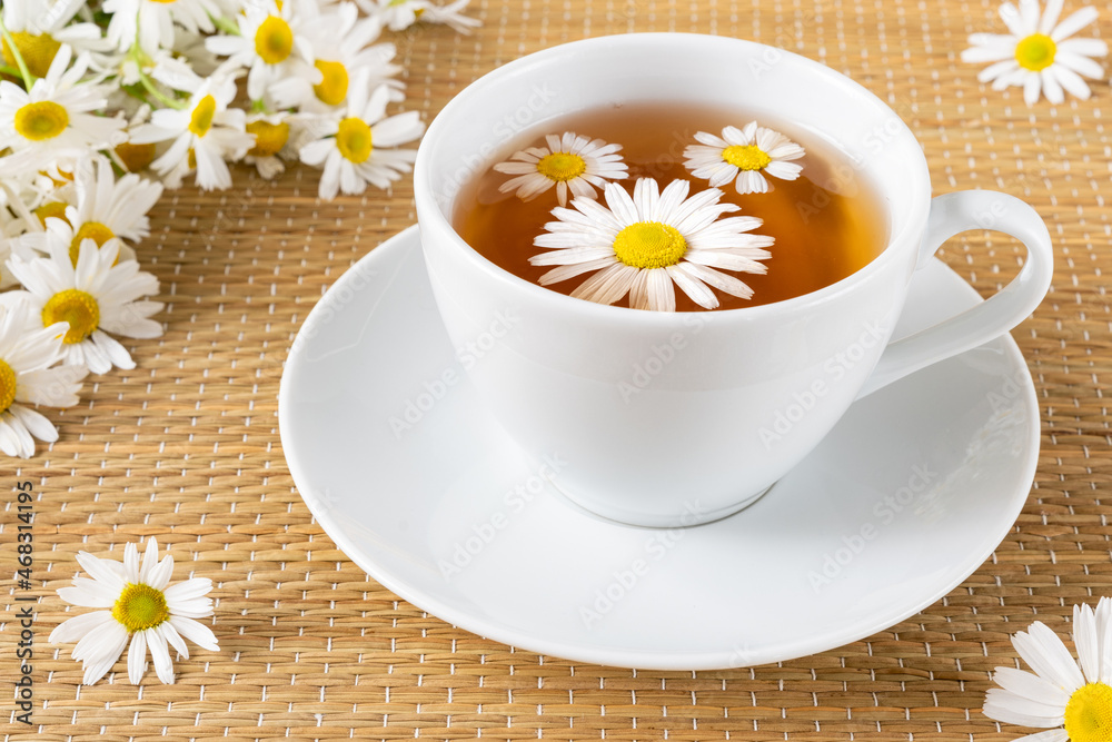 Healthy herbal tea in porcelain teacup with chamomile flowers on rattan matting Healthy herbal tea in porcelain teacup with chamomile flowers on rattan matting