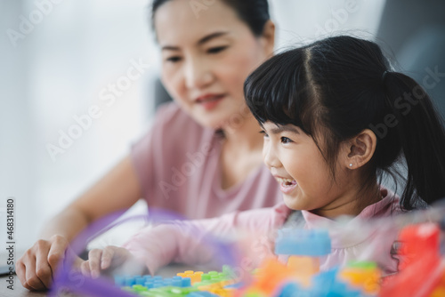 Cute little Asian girl playing alone with lego game blocks on table trying to build a new object while relaxing and enjoying