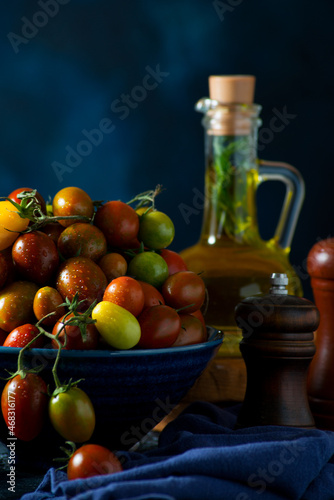Fresh organic cherry tomatoes on a branch, colorful seasonal tomatoes in a bowl on a dark background