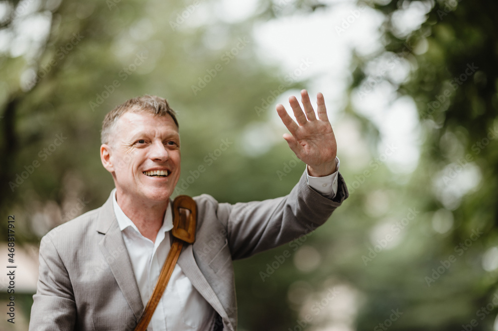 Cheerful mature businessman in formal clothing with bag waving and shouting out to someone in distance while travelling to office Cheerful mature businessman in formal clothing with bag waving and shouting out to someone in distance while travelling to office