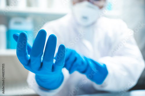Closeup of hands of a young unrecognizable scientist, researcher and doctor wearing blue hand gloves with white PPE kit and uniform with covid-19 face protection mask for safety in laboratory