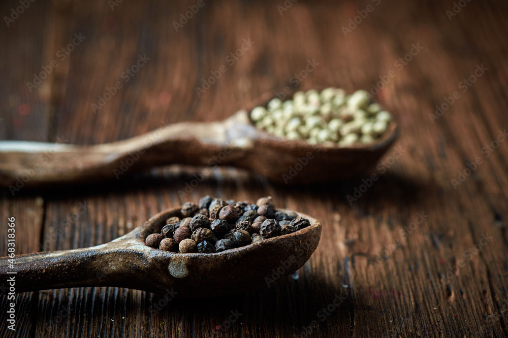 Fototapeta premium Black and white pepper on an ceramic spoon over wooden backround