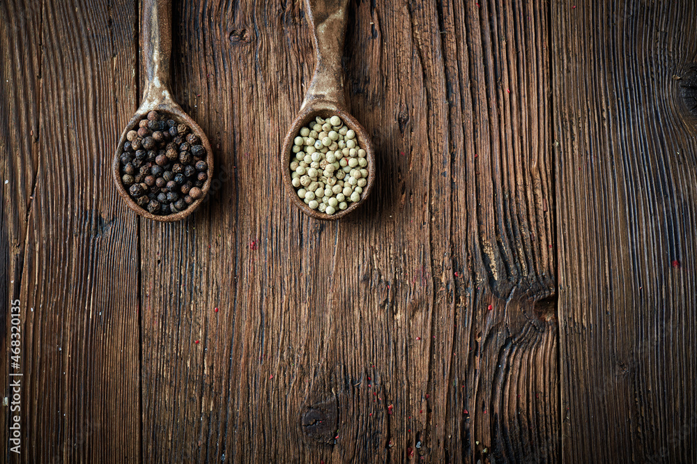 Black and white pepper on an ceramic spoon over wooden backround Black and white pepper on an ceramic spoon over wooden backround