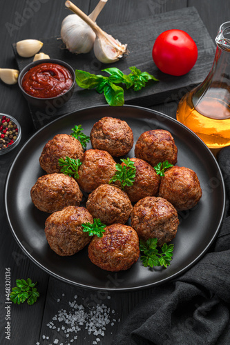 Meat Meatballs with fresh basil close-up in a black plate on a dark background.