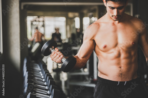 Handsome young shirtless man practicing and lifting weights for cardio and building body with abs at modern gym for fitness and healthy lifestyle