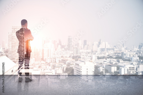 Back view of young european man standing on abstract rooftop white city background with mock up place. Success and leadership concept. Double exposure.