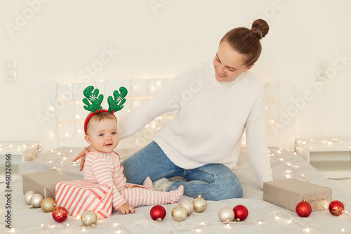 Indoor shot of happy family sitting on bed with baubles Christmas decoration, playing together, spending new year eve with good mood, New year eve celebration.