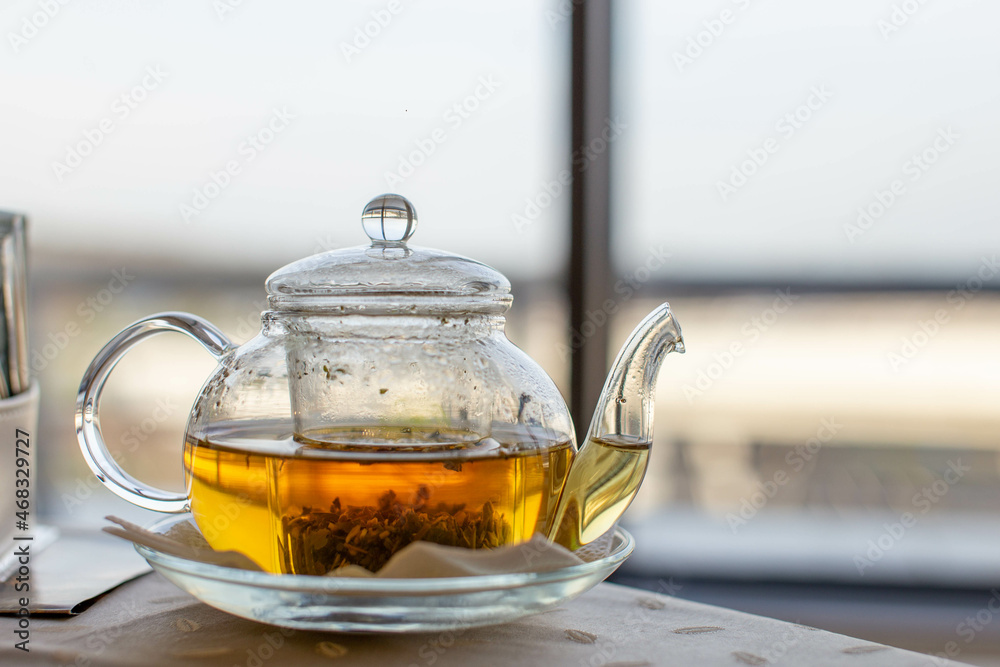 Close-up of a transparent teapot with natural herbal tea. Alternative medicine. Health care. On the right is a place to insert text, a copy of the space. Large bright window of the airport. Hot tea. Close-up of a transparent teapot with natural herbal tea. Alternative medicine. Health care. On the right is a place to insert text, a copy of the space. Large bright window of the airport. Hot tea.