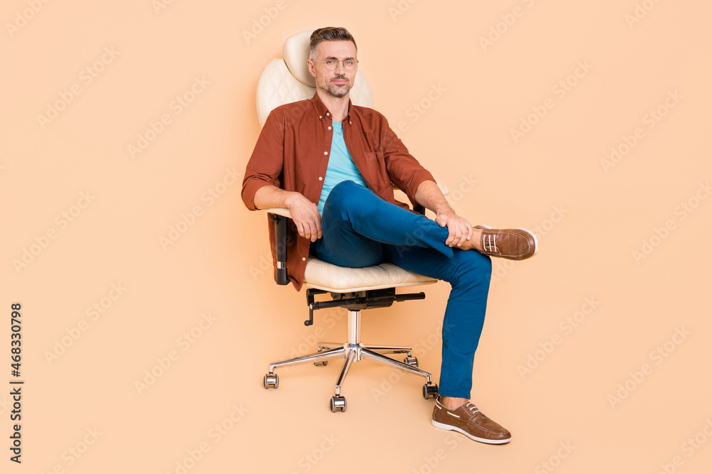 Full length photo of bossy smart partner middle-aged guy sit leather chair isolated over pastel beige color background Full length photo of bossy smart partner middle-aged guy sit leather chair isolated over pastel beige color background