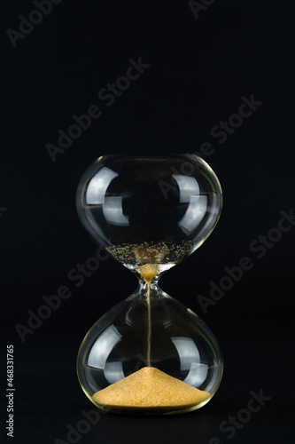 Hourglass with golden sand and black background, copy space