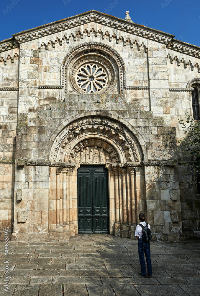 a man contemplates the Romanesque portal with archivolts and the tympanum with sculptures of biblical scenes