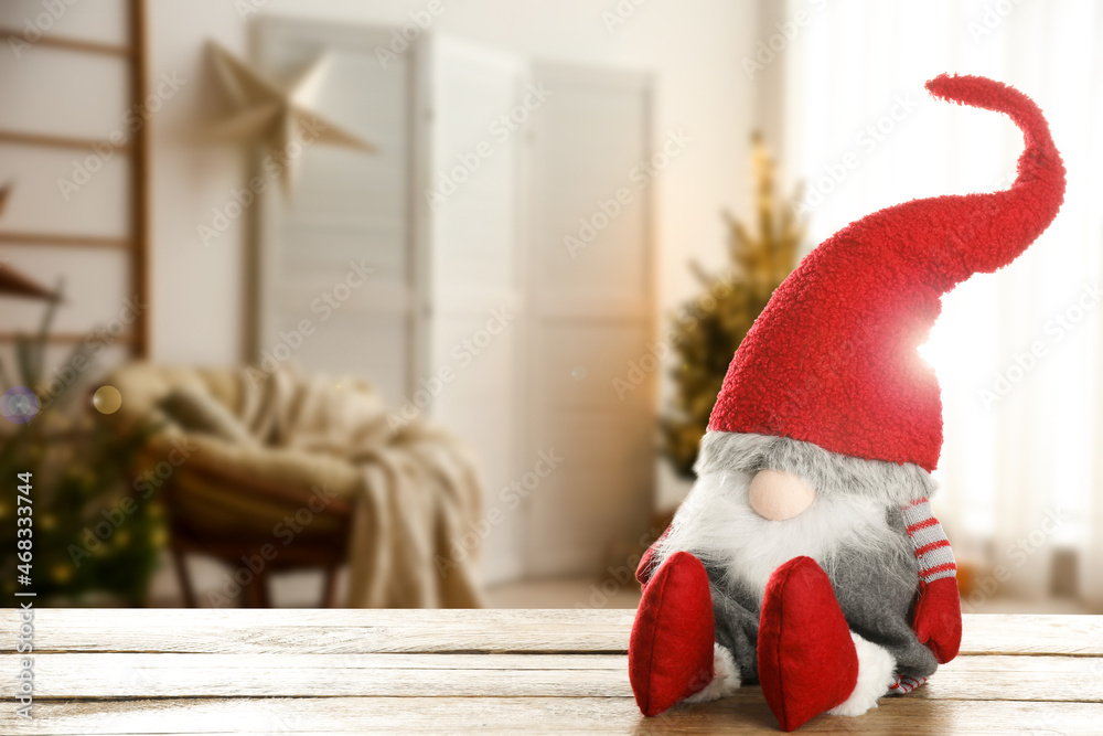 Fototapeta premium Funny Christmas gnome on wooden table in room with festive decorations. Space for text