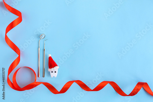 dental christmas, new year concept. toy tooth in red santa hat, medical instrument for examining oral cavity, mirror and probe on blue background. copy space, text
