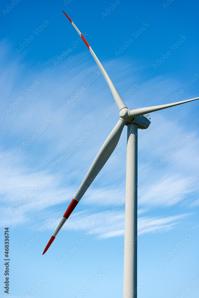 White and red wind turbine against a blue sky with clouds and copy space. Renewable energy concept.