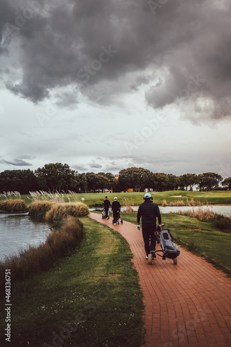 Players walking across a bridge between lakes on a golf course on a cloudy day