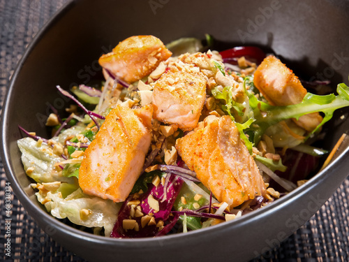 mix of green salad with fried salmon fillet and nuts in dark bowl