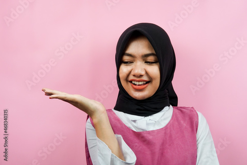 Close-up of beautiful young muslim woman with hands presenting something on empty space isolated © MunirSr