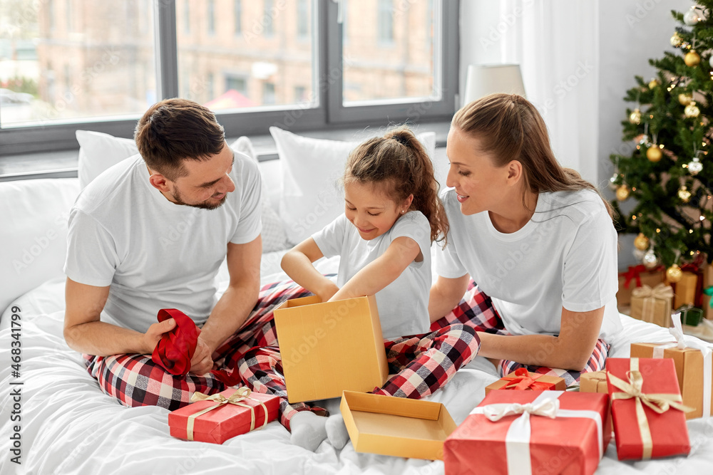 family, winter holidays and people concept - happy mother, father and little daughter opening christmas gifts in bed at home family, winter holidays and people concept - happy mother, father and little daughter opening christmas gifts in bed at home