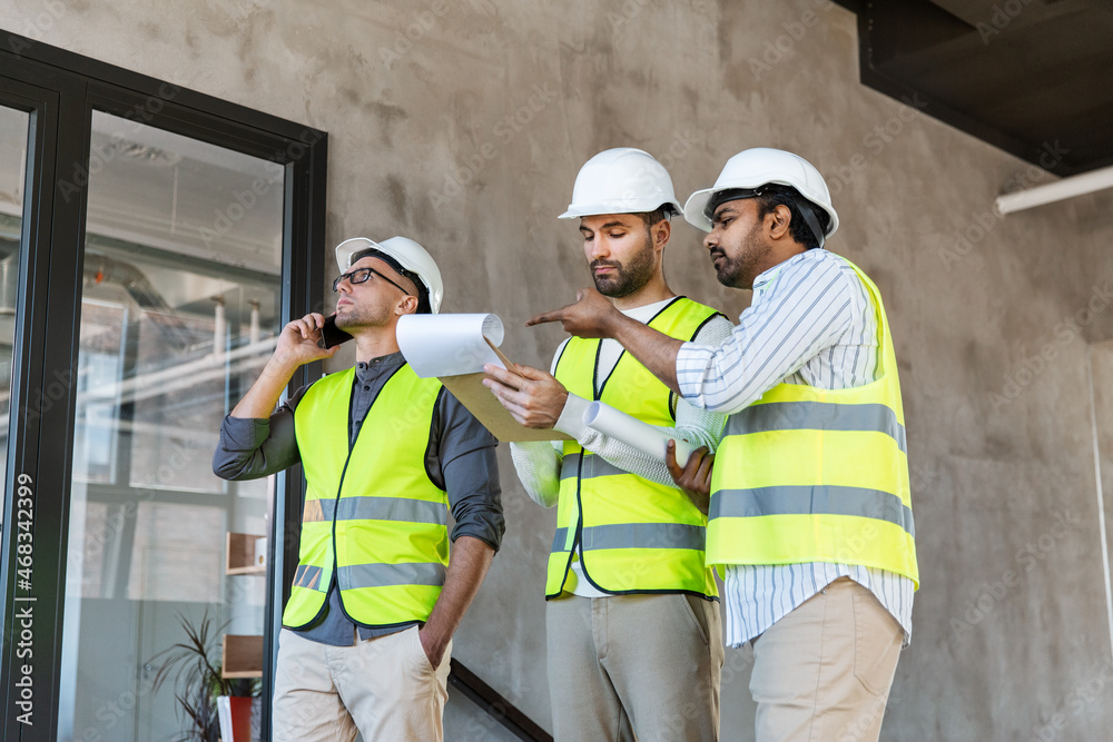 architecture, construction business and people concept - male architects in helmets with smartphone, clipboard and blueprint working at office architecture, construction business and people concept - male architects in helmets with smartphone, clipboard and blueprint working at office